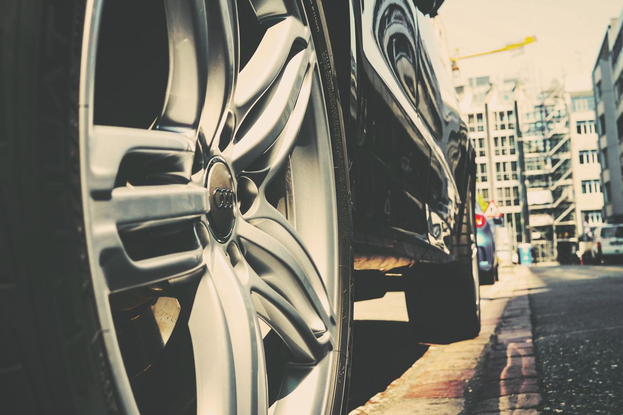 Detail of a car wheel on a city street with buildings in the background. Urban vibe.