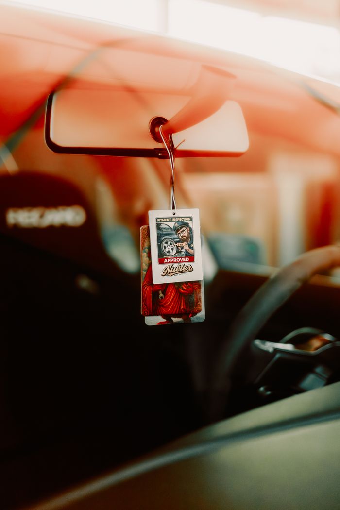 Close-up of a car interior with a dangling air freshener and steering wheel, warm tones.